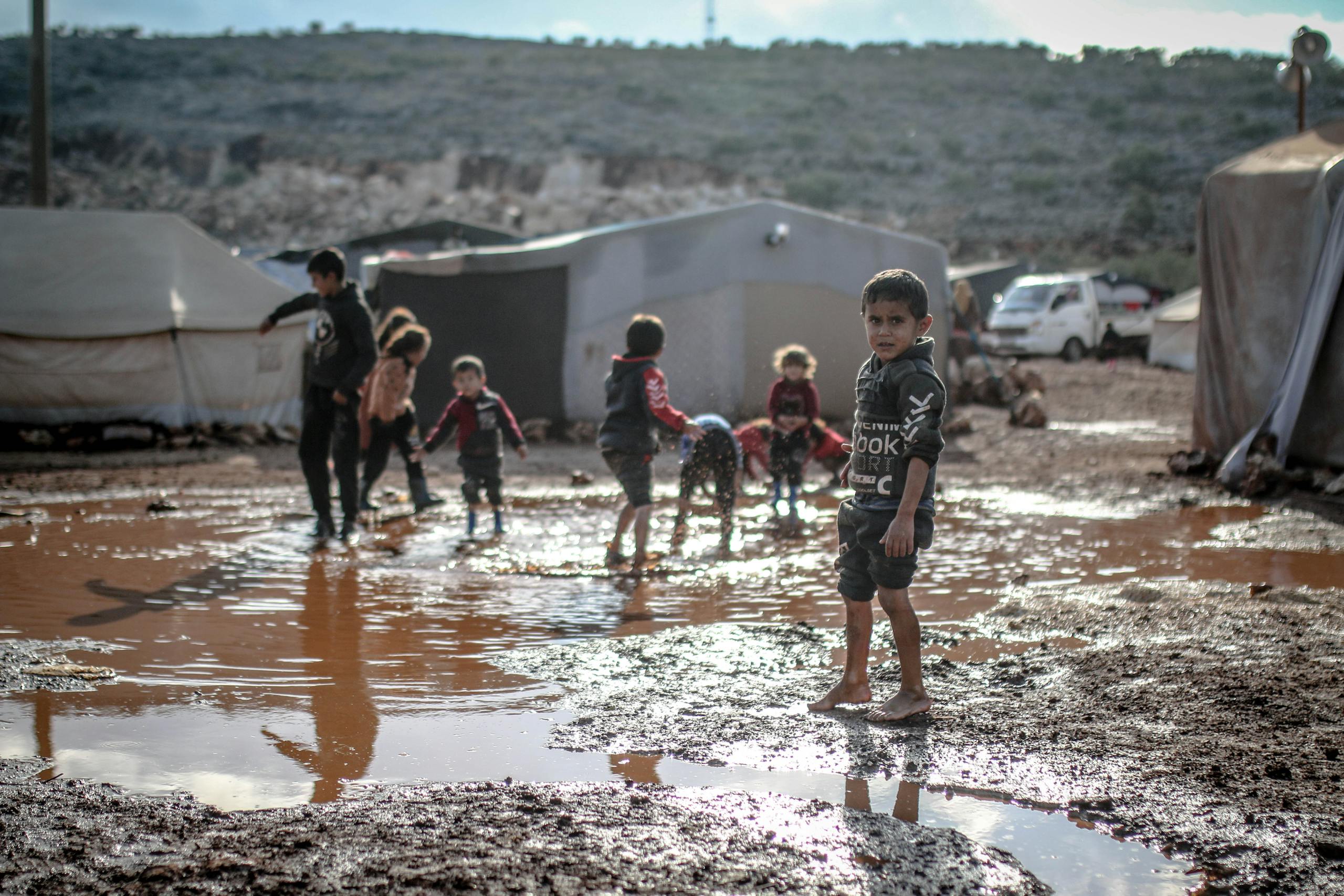 Children enjoy playing in muddy puddles at a refugee camp in Idlib, Syria.